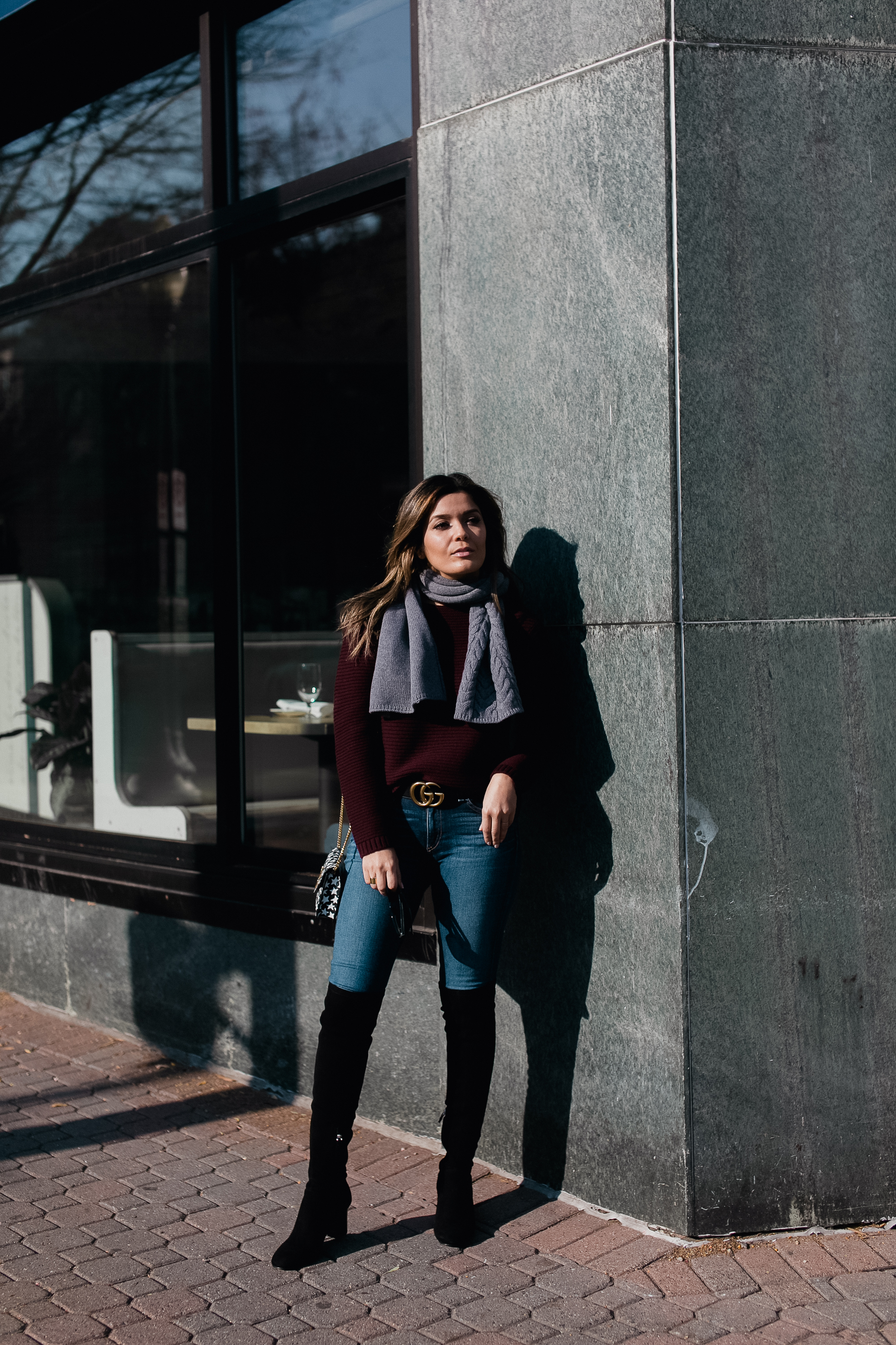 Blogger Sara Azani of Style MBA, a petite brunette woman with blonde highlights, poses outside and wears a Lafayette 148 NY cashmere sweater, Lafayette 148 NY merino cable scarf, and Lafayette 148 NY OTK or over-the-knee boots, along with Céline sunglasses, and a black Gucci belt as part of her burgundy and grey outfit.
